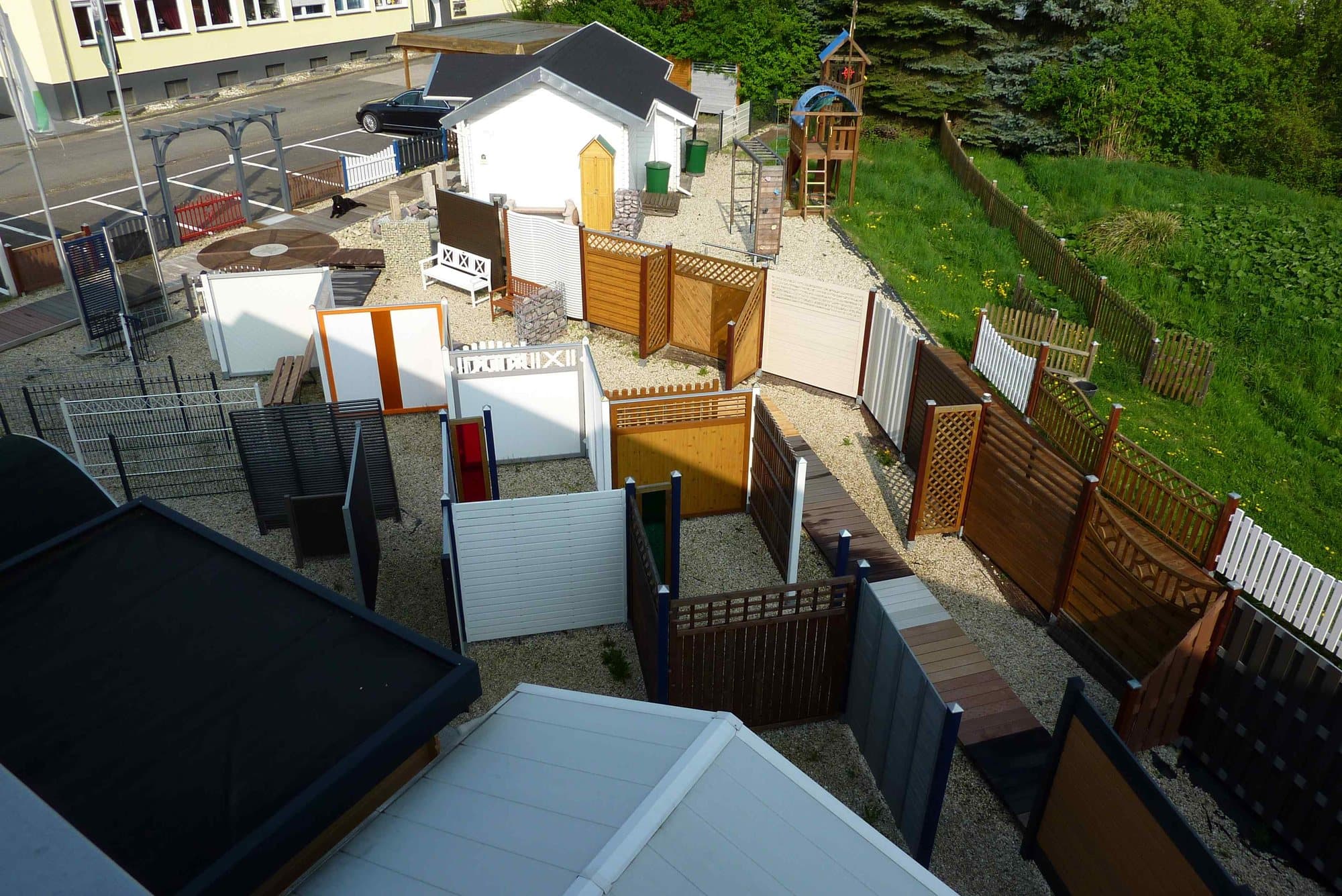 Blick von oben auf die Außenausstellung mit Zäunen, Gartenhäusern und Spielturm